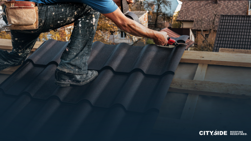 Roofer installing black metal roofing tiles on a residential roof