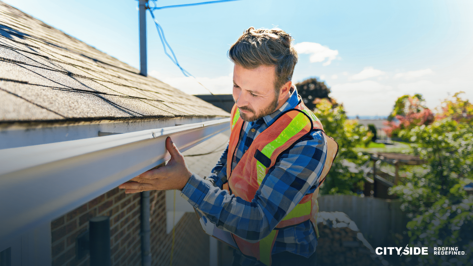 A man in a safety vest is diligently working on a gutter, ensuring proper maintenance and safety measures are in place.