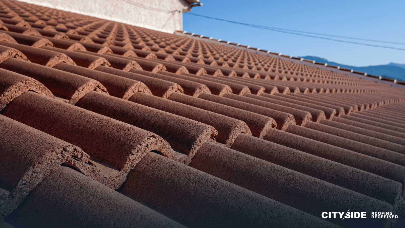 A close-up view of a red-tiled roof, showcasing the texture and arrangement of the tiles against a clear sky.