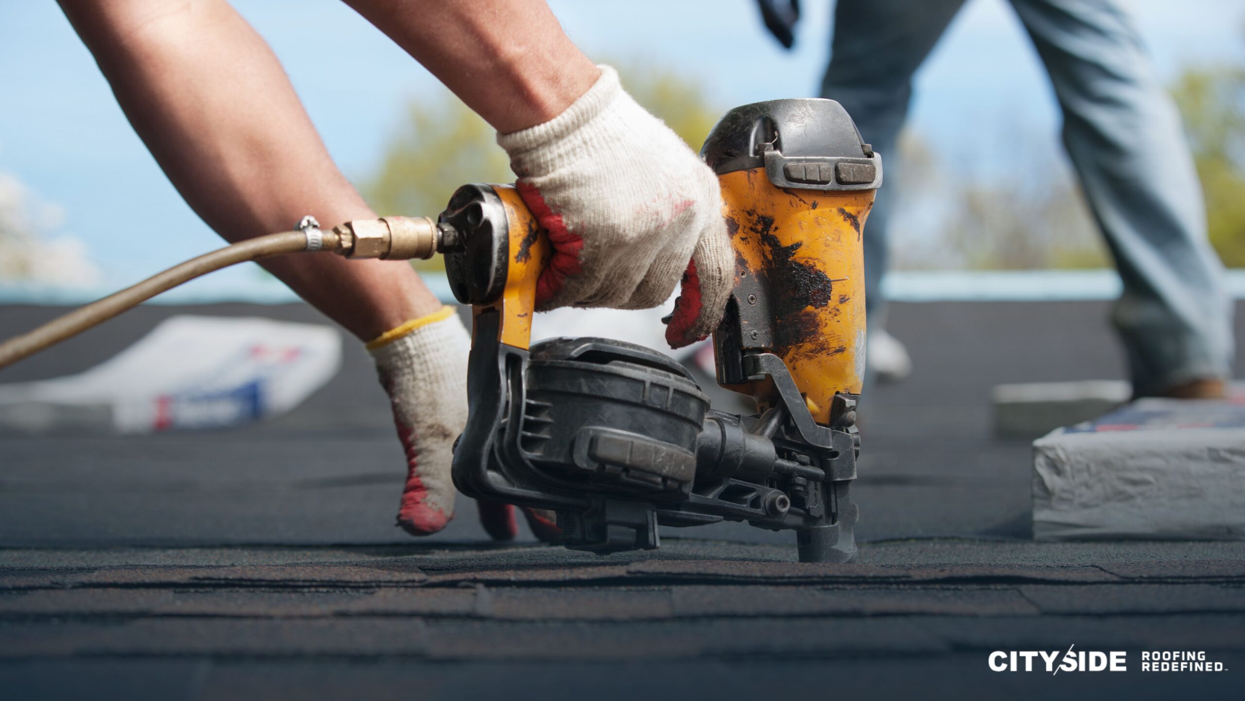 A person operates a nail gun while installing roofing materials on a house, demonstrating skilled construction work.