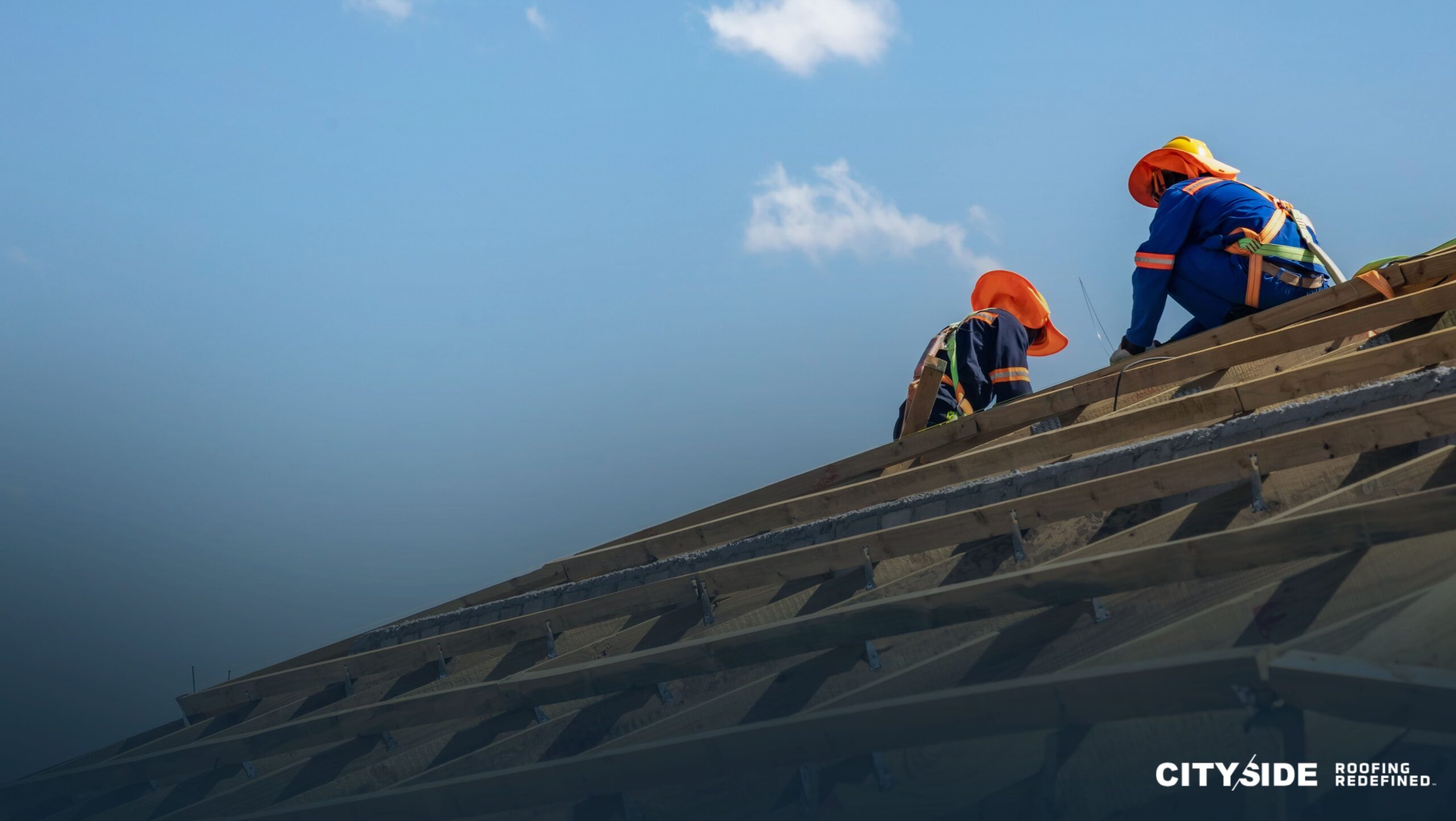 Two men are collaborating on a roof under a clear blue sky, focused on their work and safety measures.