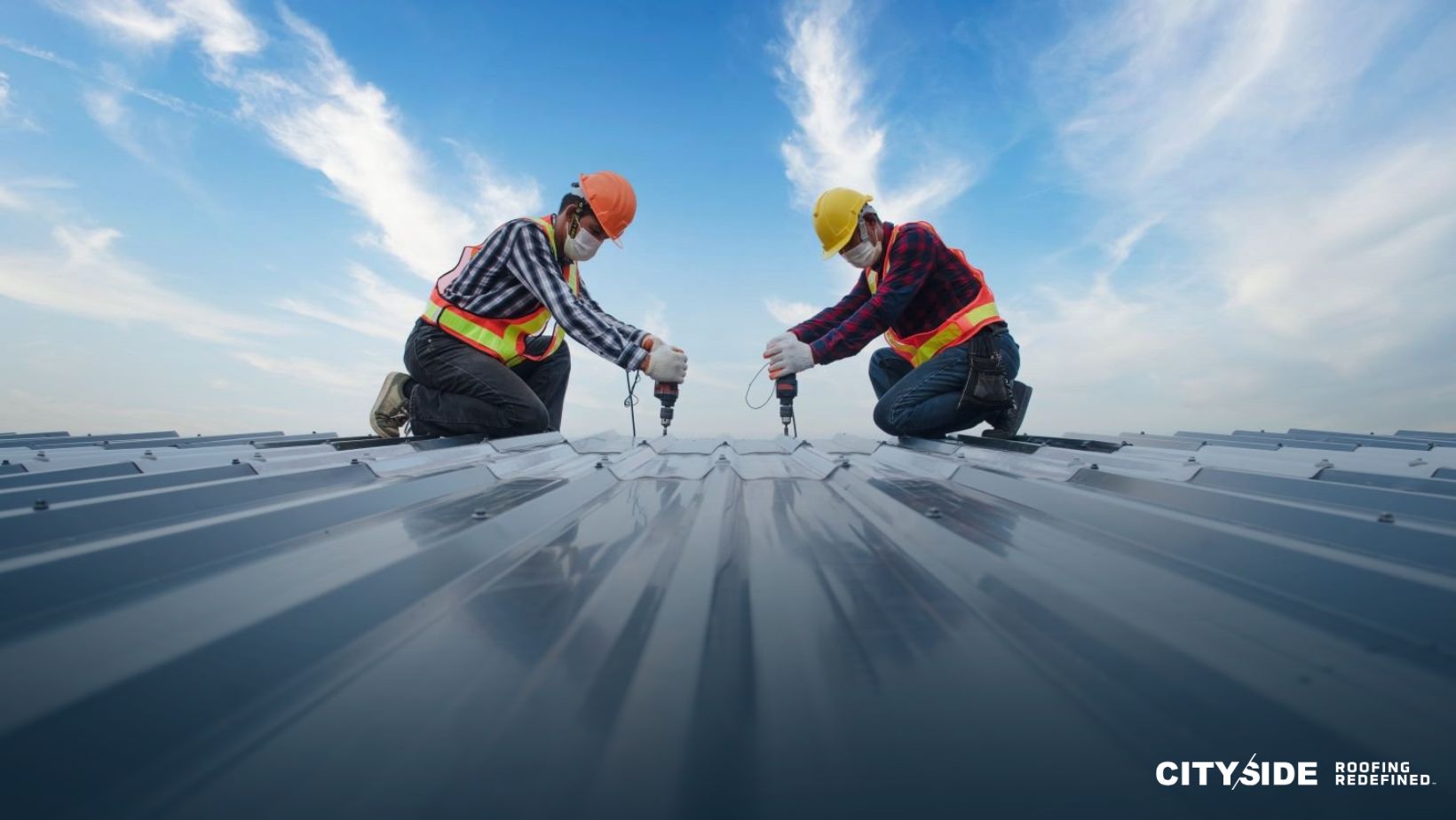 Two men installing a metal roof, focused on their work while using tools and safety equipment.