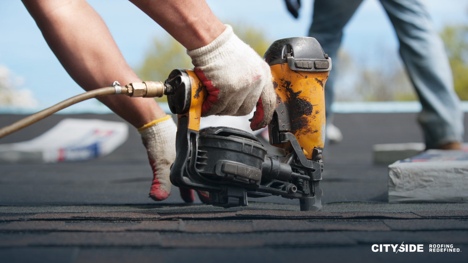 A person operates a nail gun while installing roofing materials on a house.