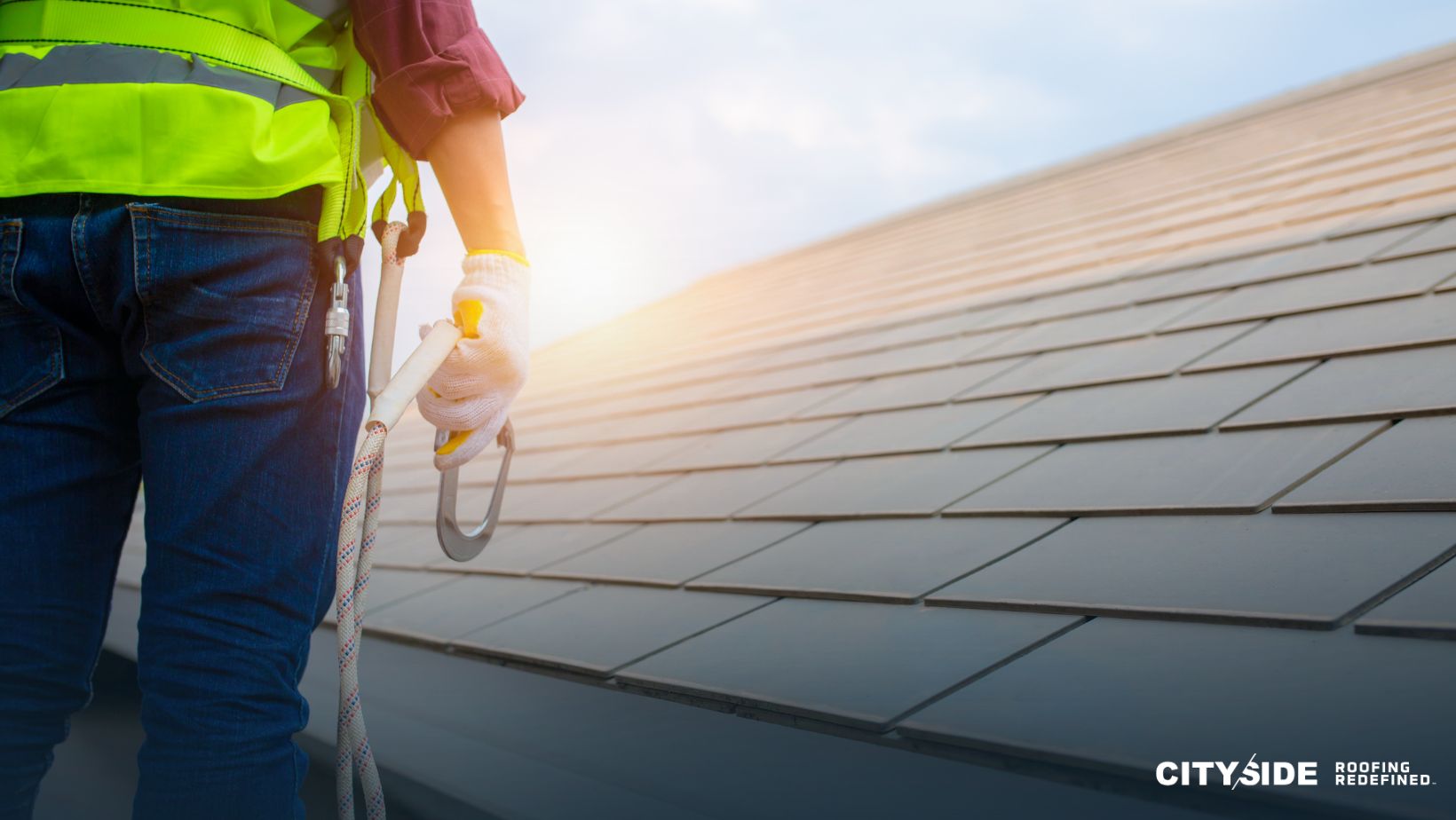 A man wearing a safety vest stands on the roof of a house