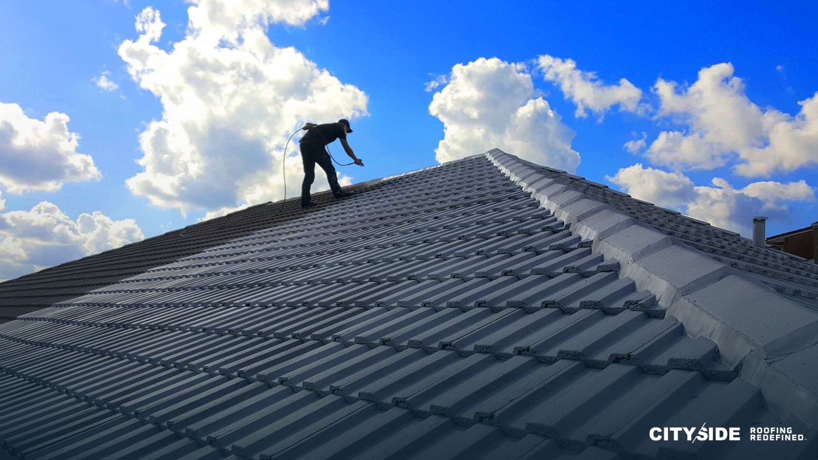 A man stands on a house roof under a clear blue sky