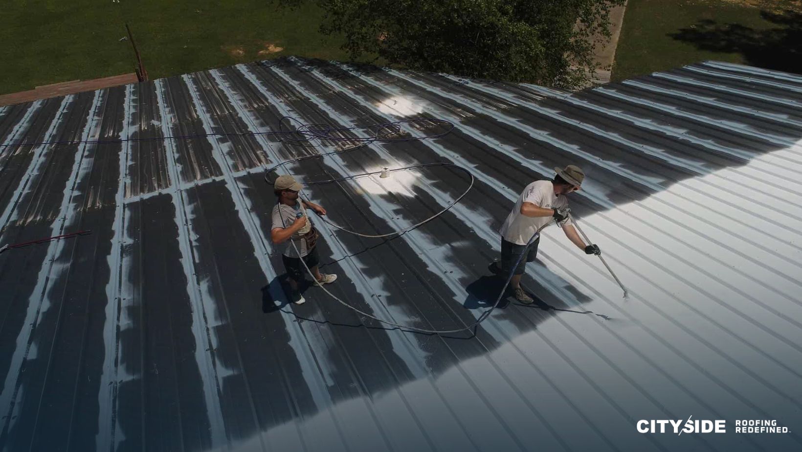 Two workers applying roof coating on a house roof