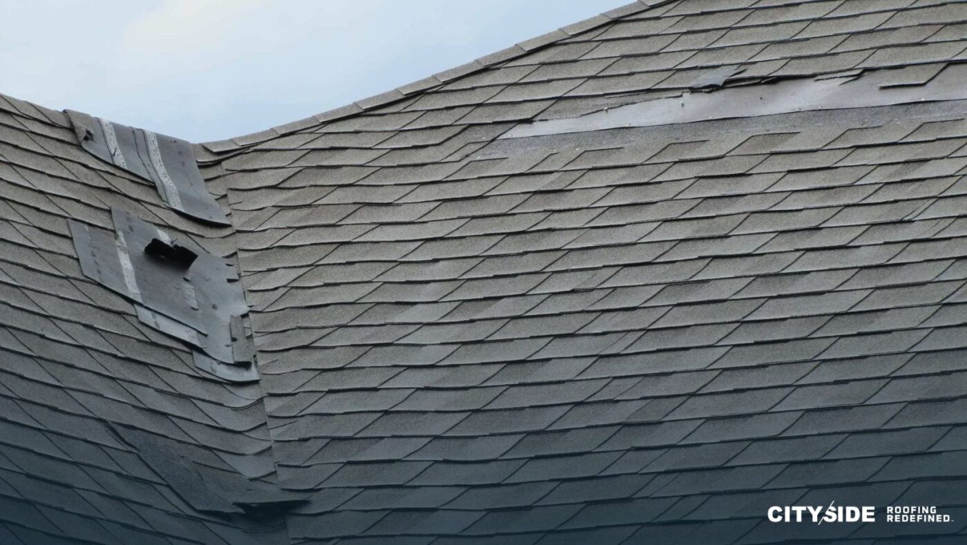 A close-up of a roof with a missing shingle and a shattered window