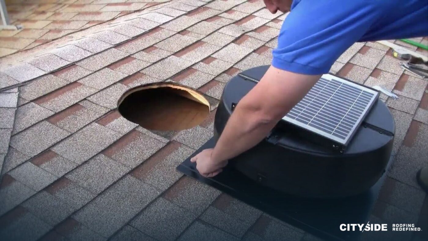 A man installs a solar panel on a sloped roof under a clear blue sky.