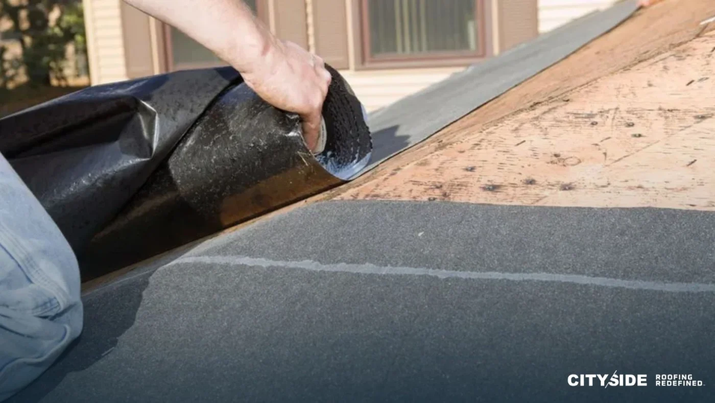 A man installs roofing material on a residential roof, focused on his task.