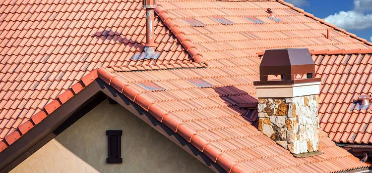 A red tile roof featuring a chimney at its peak against a clear blue sky.
