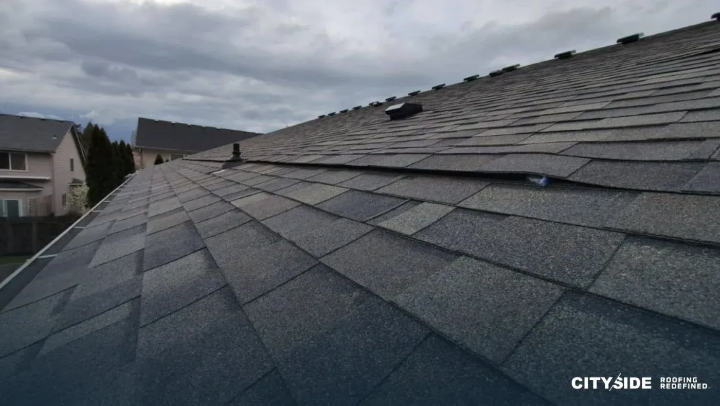 A close-up of a roof featuring a single shingle, highlighting its texture and color against the sky.