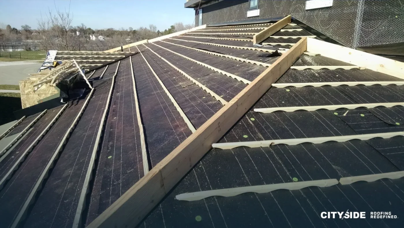 A worker installing a metal roofing system on a sloped roof under clear blue skies
