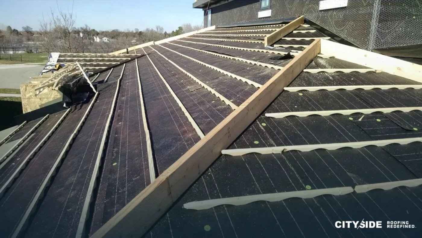 A worker installing a metal roofing system on a sloped roof under clear blue skies