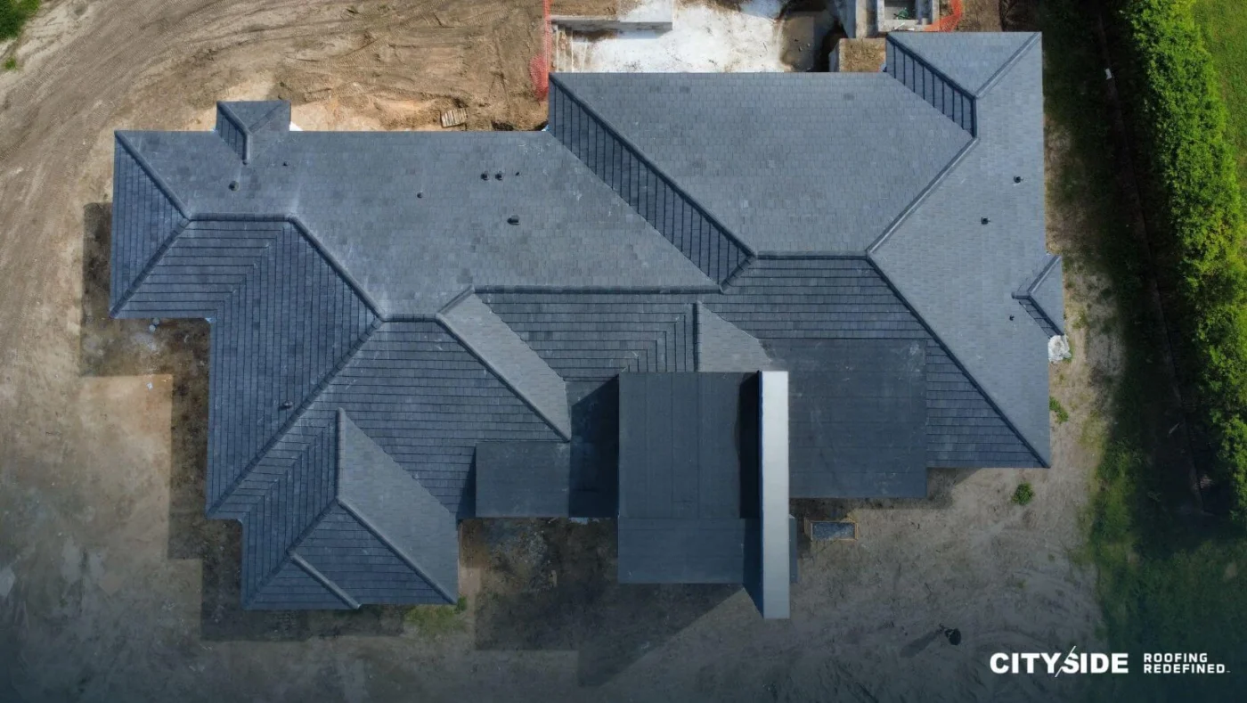 Top-down perspective of a house with a distinct roof, surrounded by greenery.