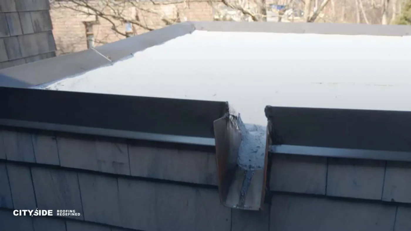 A flat roof corner with a metal flashing, showing the joint where two roof sections meet.