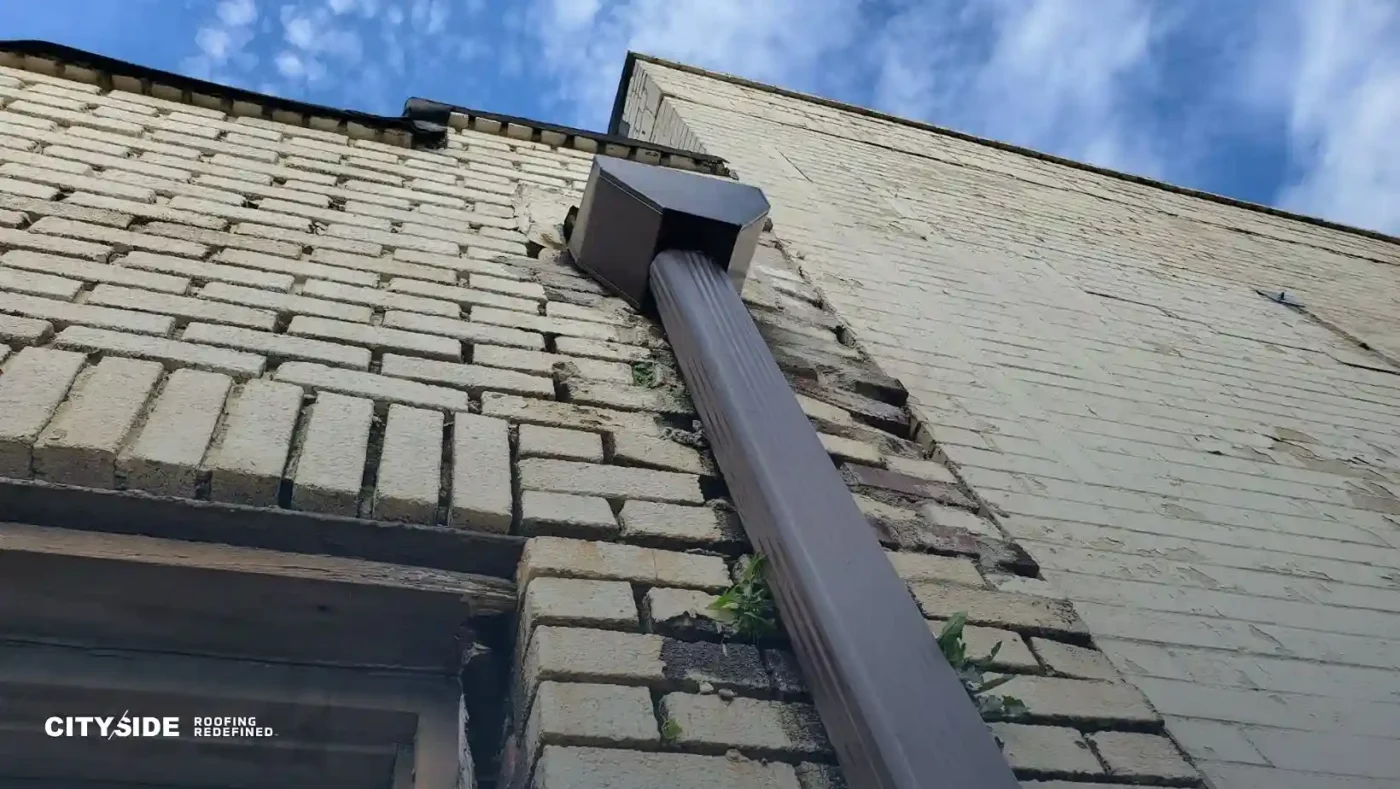 Side view of a brick building with a visible metal pipe mounted on the exterior.