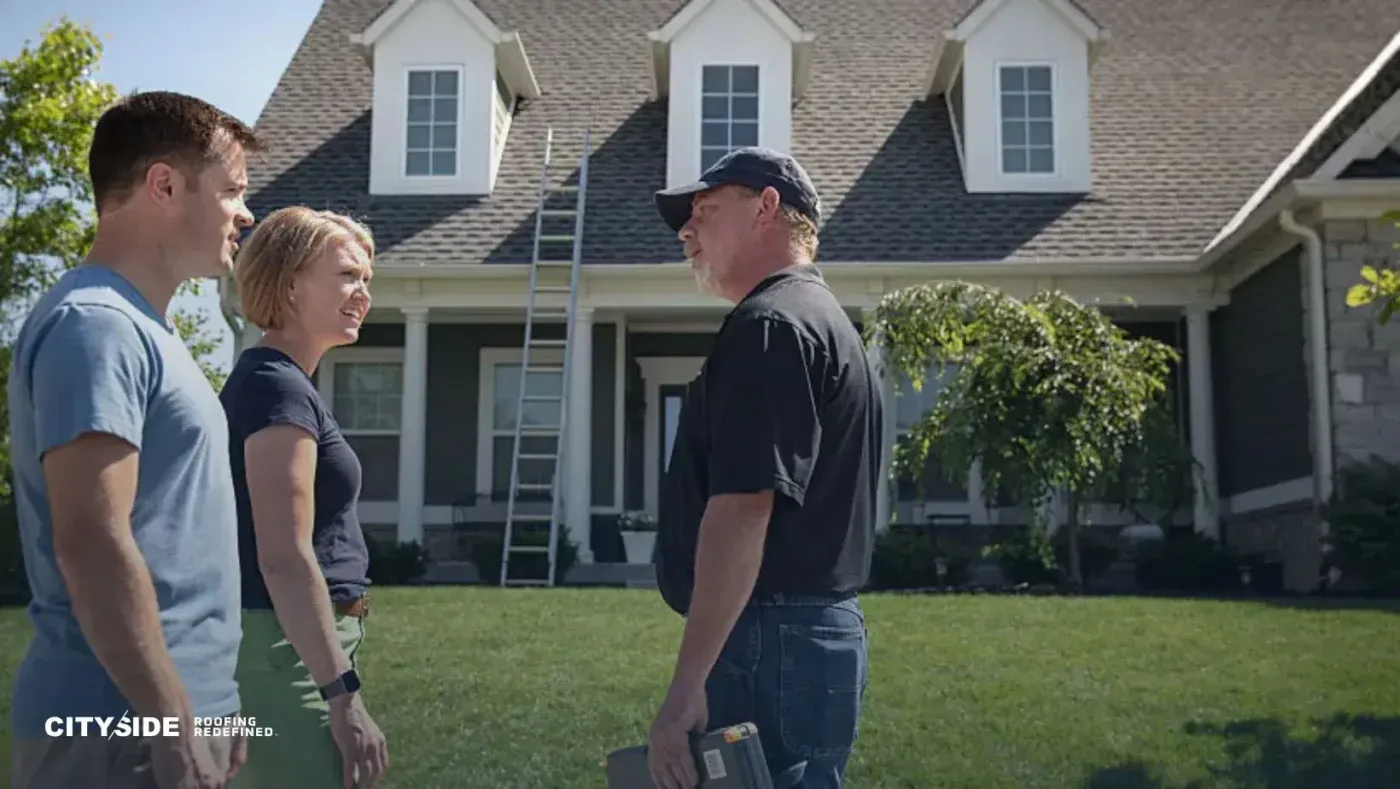 A couple smiles while talking to a worker in front of a suburban house with a pitched roof and dormer windows. A ladder leans against the house.