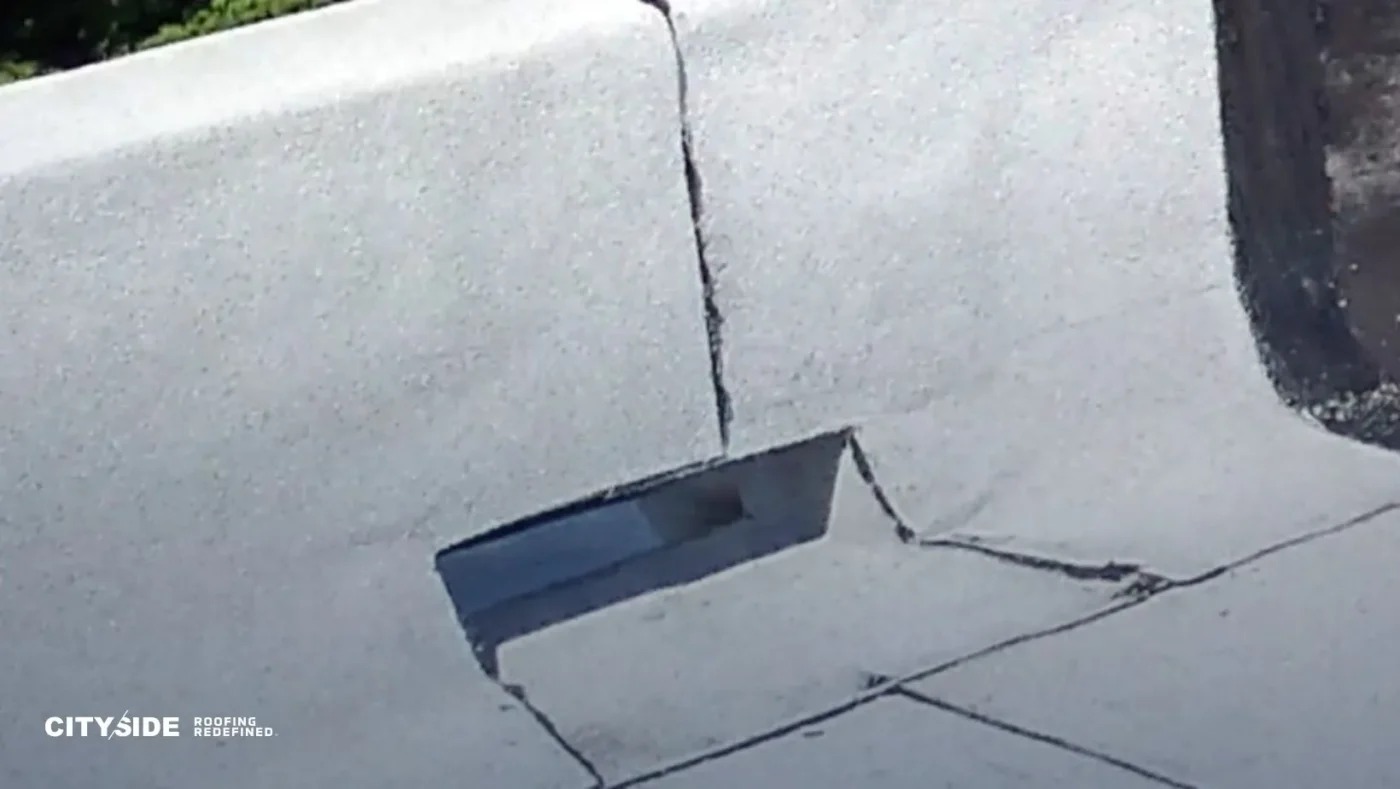 Close-up of a damaged flat rooftop with a crack extending from a large gap on the surface. Uneven surfaces suggest wear and the need for repair.