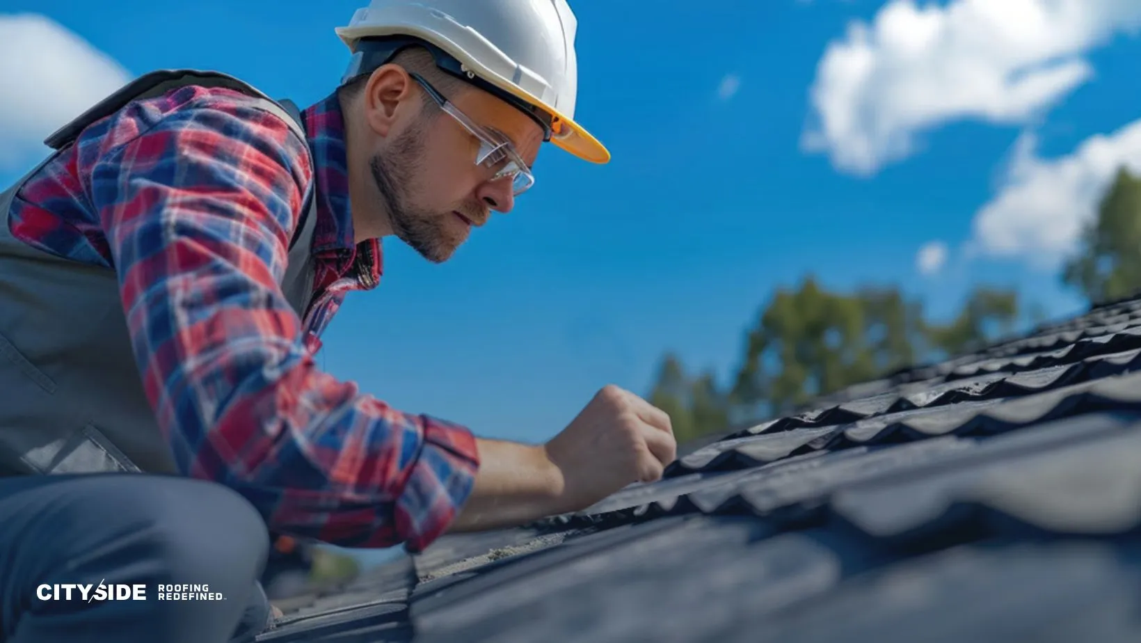 A man in a hard hat and plaid shirt inspects roofing shingles under a bright blue sky with scattered clouds, conveying focus and professionalism.