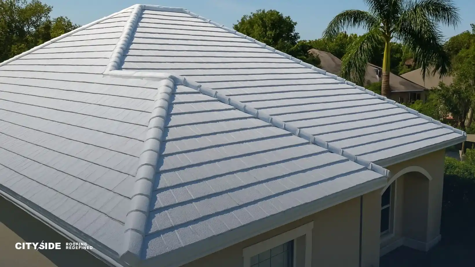 A modern house with a sleek, white tiled roof under clear skies. Surrounded by lush greenery and palm trees, conveying a tropical, serene vibe.