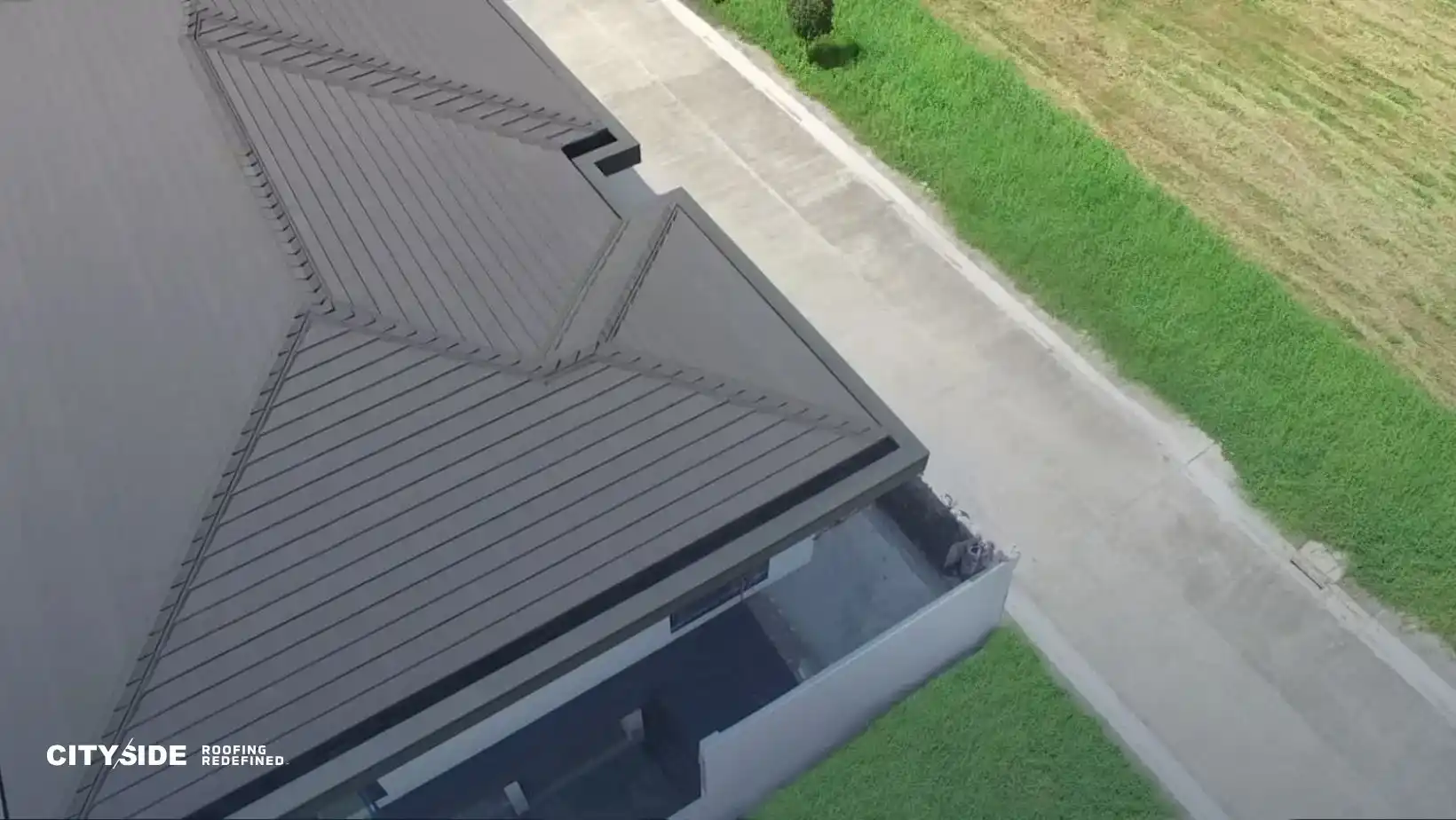 Aerial view of a modern building's roof with geometric patterns, bordered by a gray road and green grass, conveying a sense of sleek design and order.