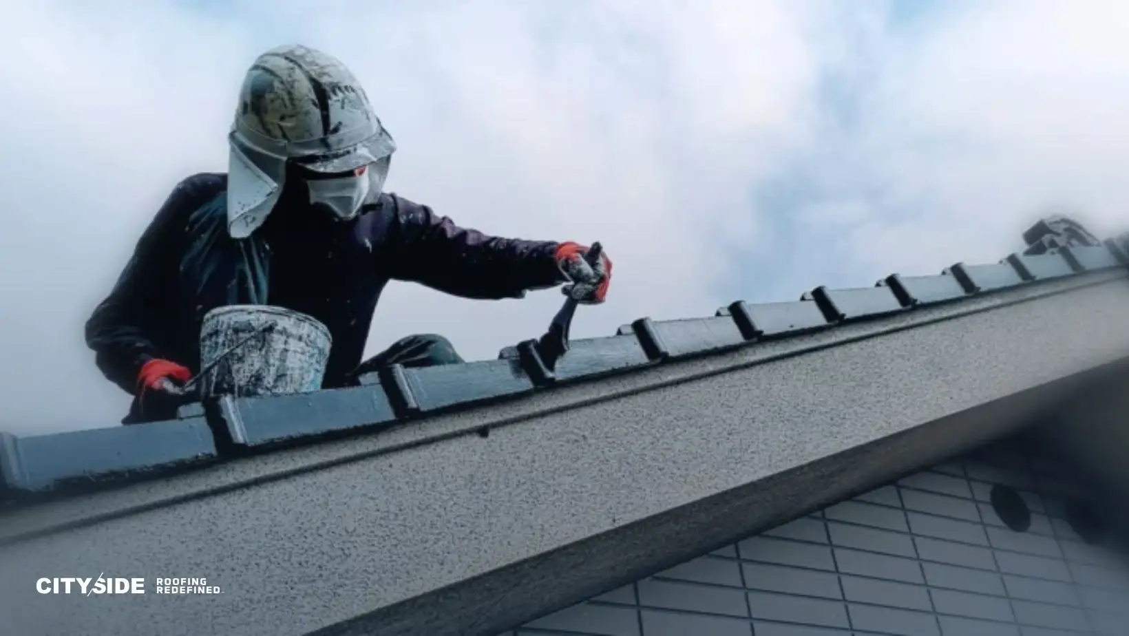 A worker in protective gear applies black paint to a sloped roof under a cloudy sky, conveying determination and craftsmanship. "CitySide Roofing" logo visible.
