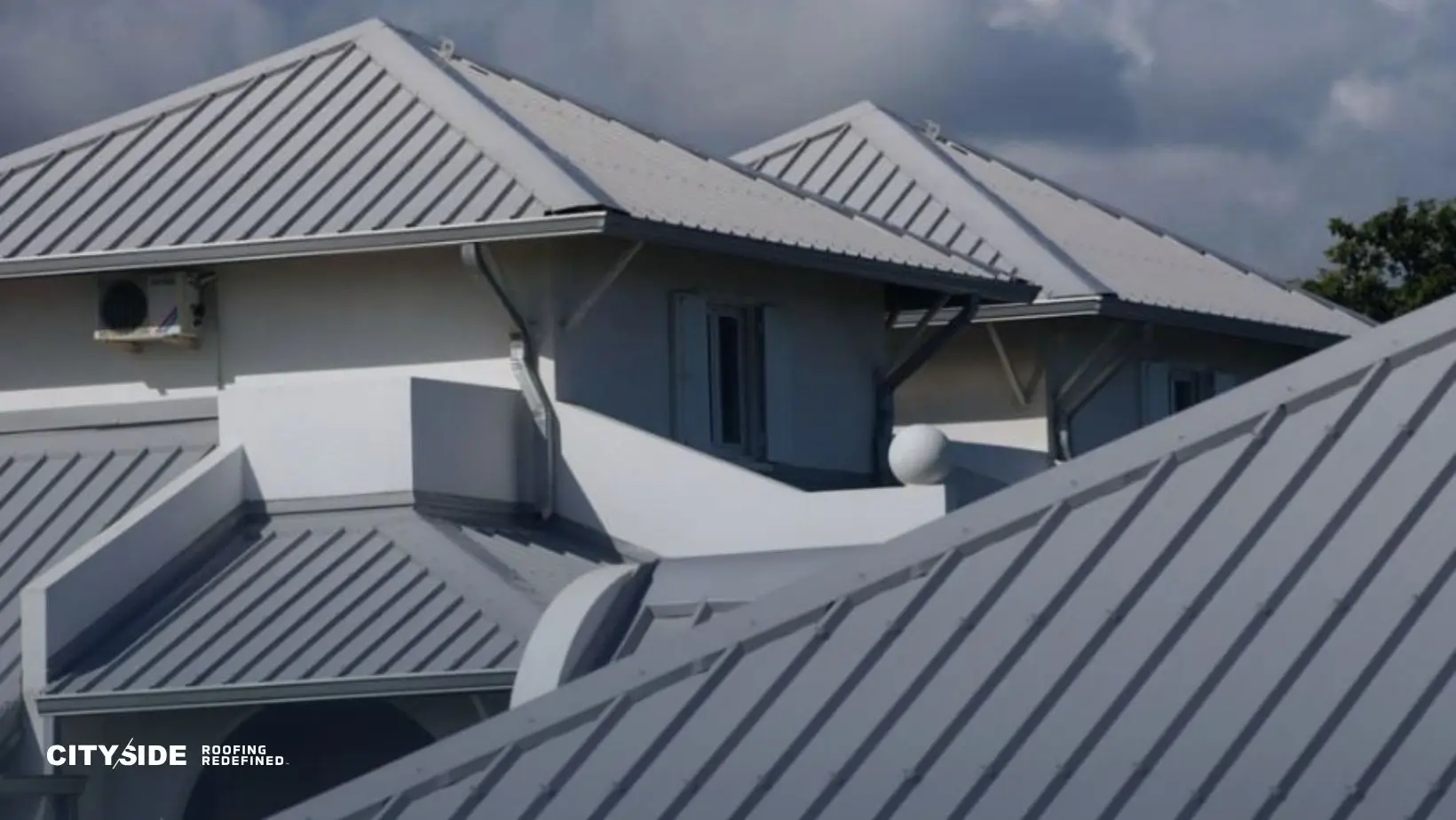 A cluster of buildings with sleek, modern metal roofs under a clear sky, conveying a sense of durability and contemporary design. Rooftop details and shadows create a dynamic look.