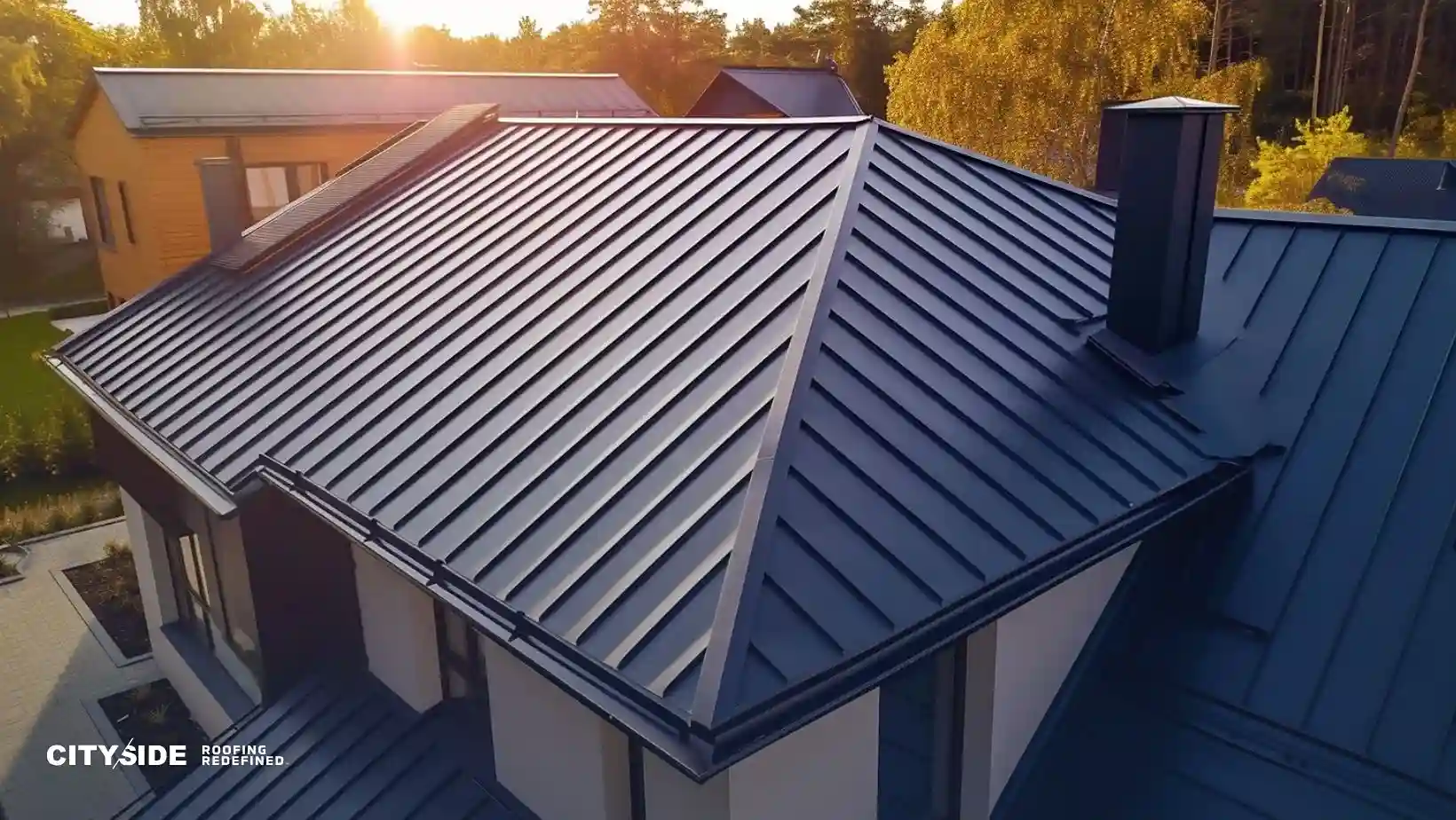 A modern house features a sleek, dark metal roof against a backdrop of sunset-lit trees, conveying a sense of durability and contemporary style.