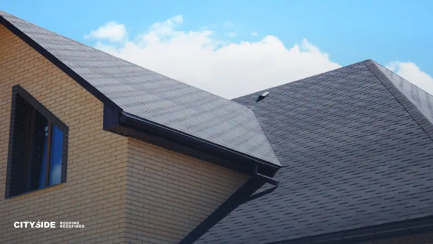 Modern house with dark gray shingled roof against a blue sky, features light brick walls and a single window, conveying a sense of durability.