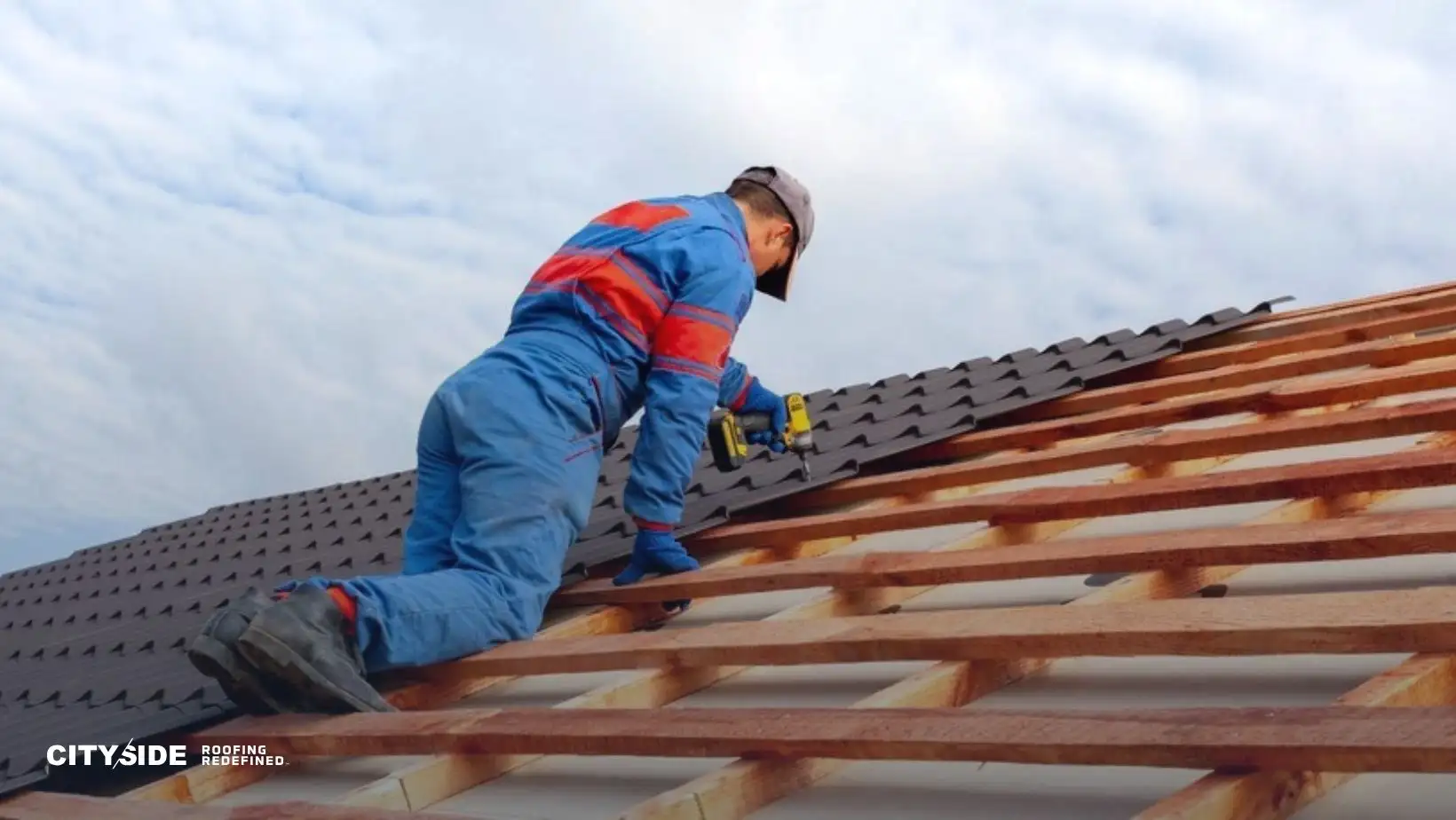 A worker in blue overalls and a cap installs shingles on a roof, using a drill. The sky is partly cloudy, conveying a focused, determined mood.